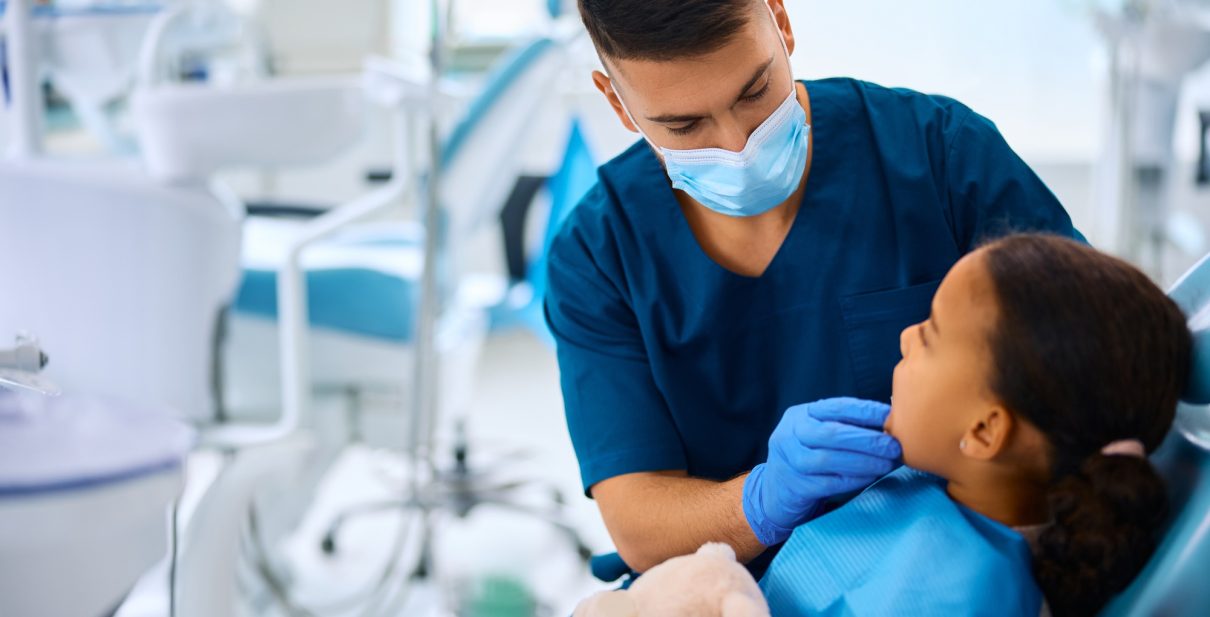 Dentist examining teeth of little black girl at dental clinic.