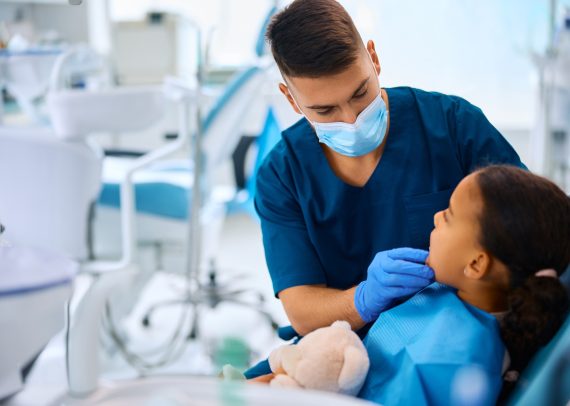 Dentist examining teeth of little black girl at dental clinic.